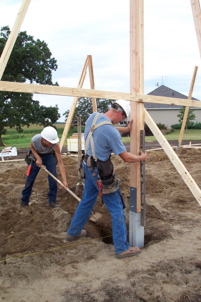 Workers set a permacolumn precast post into a hole while constructing a pole barn